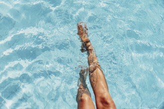 Two legs dipping in the sunny blue pool water, relaxed atmosphere