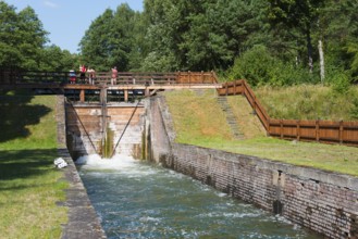 Brick and wooden sluice with people and surrounding greenery in a summer atmosphere, Sluza Paniewo,