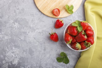 Fresh red strawberry in white bowl on gray concrete background. top view, copy space, flat lay