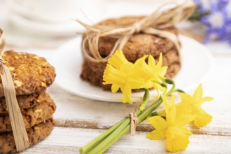 Oatmeal cookies with spring snowdrop flowers bluebells, narcissus and cup of coffee on white wooden