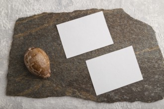 White paper business card, mockup with natural stone and seashell on gray concrete background.