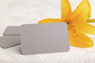 Gray paper business card mockup with orange day-lily flower on gray concrete background. Blank,