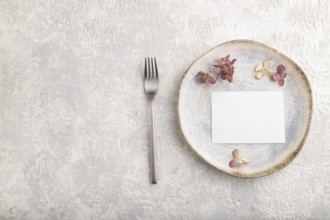 White paper invitation card, mockup with dried hydrangea flowers on ceramic plate and gray concrete