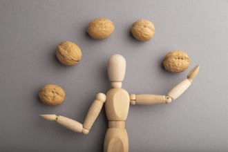 Wooden mannequin juggling walnuts on gray pastel background. close up, isolated, delivery concept