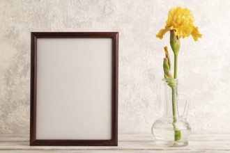 Wooden frame with yellow iris flower in glass on gray concrete background. side view, copy space,