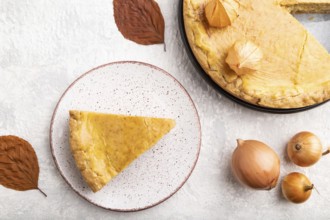 Autumn onion pie decorated with leaves and cup of coffee on gray concrete background. Top view,