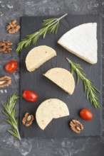 Cheddar cheese and various types of cheese with rosemary and tomatoes on black slate board on a