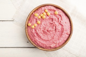 Hummus with beet in wooden bowl on a white wooden background and linen textile. Top view, flat lay,