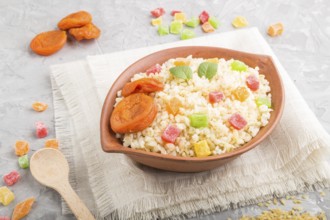 Bulgur porridge with dried apricots and candied fruits in clay bowl on a gray concrete background