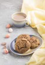 Homemade oatmeal cookies with a cup of cocoa and a yellow textile on a gray concrete background.