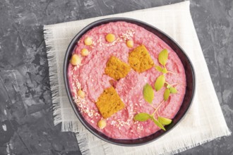 Hummus with beet and microgreen basil sprouts in ceramic bowl on a black concrete background and