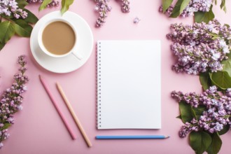 Purple lilac flowers and a cup of coffee with notebook and colored pencils on pastel pink