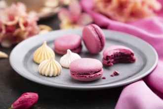 Purple macarons or macaroons cakes with cup of coffee on a black concrete background and pink