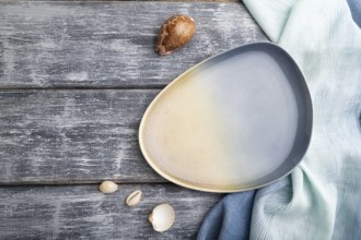 Empty blue ceramic plate on gray wooden background and blue textile. Top view, copy space, flat lay