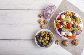 Salad with fresh cherry tomatoes, mozzarella cheese, olives, kiwi, onion and walnuts on white