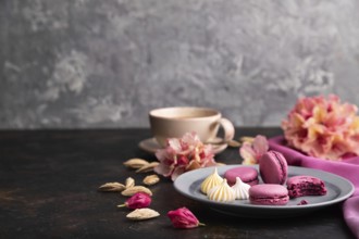 Purple macarons or macaroons cakes with cup of coffee on a black concrete background and pink