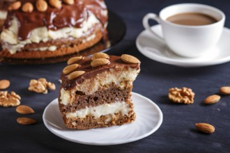 Homemade chocolate cake with milk cream, caramel and almonds on black wooden background. cup of