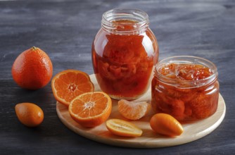 Tangerine and kumquat jam in a glass jar with fresh fruits on a black wooden table. Homemade, copy