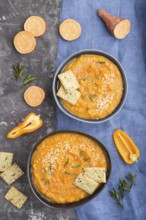 Sweet potato or batata cream soup with sesame seeds and snacks in blue ceramic bowls on a black