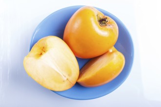 Ripe orange persimmon in a blue plate isolated on white background. closeup