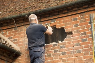 Builder removing red bricks to make window space, Suffolk, England, UK