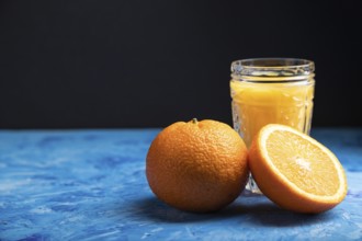 Glass of orange juice on a black and blue background. Hard light, contrast. Side view, copy space