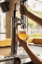 Close-up of a woman's delicate hands pouring fresh beer from a tap into a glass in a cozy pub