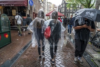 Tourists in rainy weather, with plastic ponchos, in the historic centre of Amsterdam, Netherlands