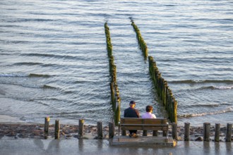 An elderly couple sitting on a bench on the beach, at high tide, breakwater, Netherlands