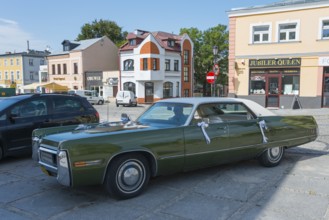 A green vintage car is parked in a sunny city street in the historic city centre, Chrysler Imperial