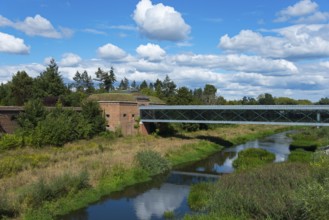 Natural landscape with a bridge over a river and lush greenery under a cloudy sky, view from the