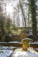 Female figure on a grave in the snow, sun from behind, Dresden Forest Cemetery, Saxony, Germany,