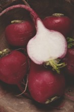 Bright red radishes lie in a rustic wooden bowl, highlighting their fresh appearance. One radish is