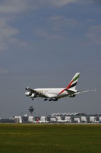 Emirates Airbus A380-800 approaching under blue sky, with control tower and Terminal 2 landing on