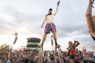 A festival visitor stands on the hands of two people during the performance of the band Feine Sahne