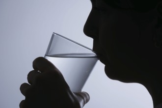 Symbolic photo on the subject of drinking water. Silhouette of a woman drinking a glass of tap