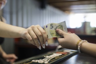 Symbol photo on the subject of cash payment in the catering trade. A woman pays with 5 euros cash