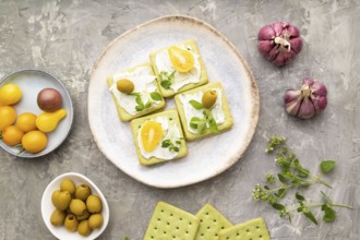 Green cracker sandwiches with cream cheese and cherry tomatoes on gray concrete background. top