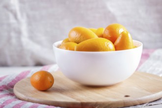 Kumquats in a white plate on a wooden kitchen board, close up