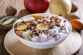 Vegetarian salad of bananas, apples, pears, kumquats, kiwi with granola and yogurt on brown woodem