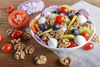 Salad with fresh cherry tomatoes, mozzarella cheese, olives, kiwi, onion and walnuts on brown