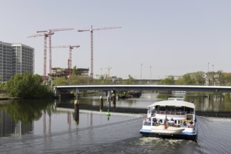 Four red construction cranes stand on a building site in Berlin's Heidestraße while a tourist boat