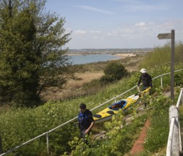 Two men carrying a canoe down to the beach, West Mersea, Mersea Island, Essex, England, United