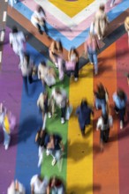 People crossing a pedestrian crossing, on a road, the road surface is colourful, in rainbow