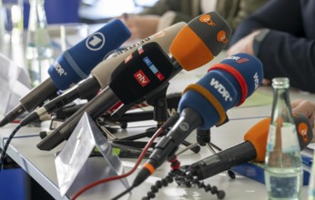 Microphones from various radio and television stations are on the table at a press conference