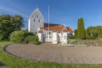 Whitewashed church in Dalby, side view, red roof, cemetery, stepped gable, entrance gate, stone