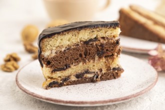 Chocolate biscuit cake with caramel cream and walnuts, cup of coffee on gray concrete background.