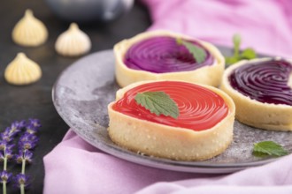 Sweet tartlets with jelly and milk cream with cup of coffee on a black concrete background and pink