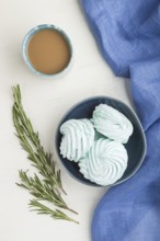 Blue colored homemade zephyr or marshmallow with cup of coffee on white wooden background with blue