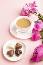 Cup of cioffee with chocolate candies, pink peony flowers on pink pastel background. side view,